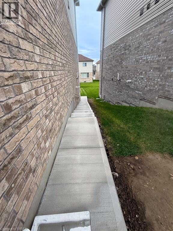 A concrete walkway leads from a brick wall to a grassy area.