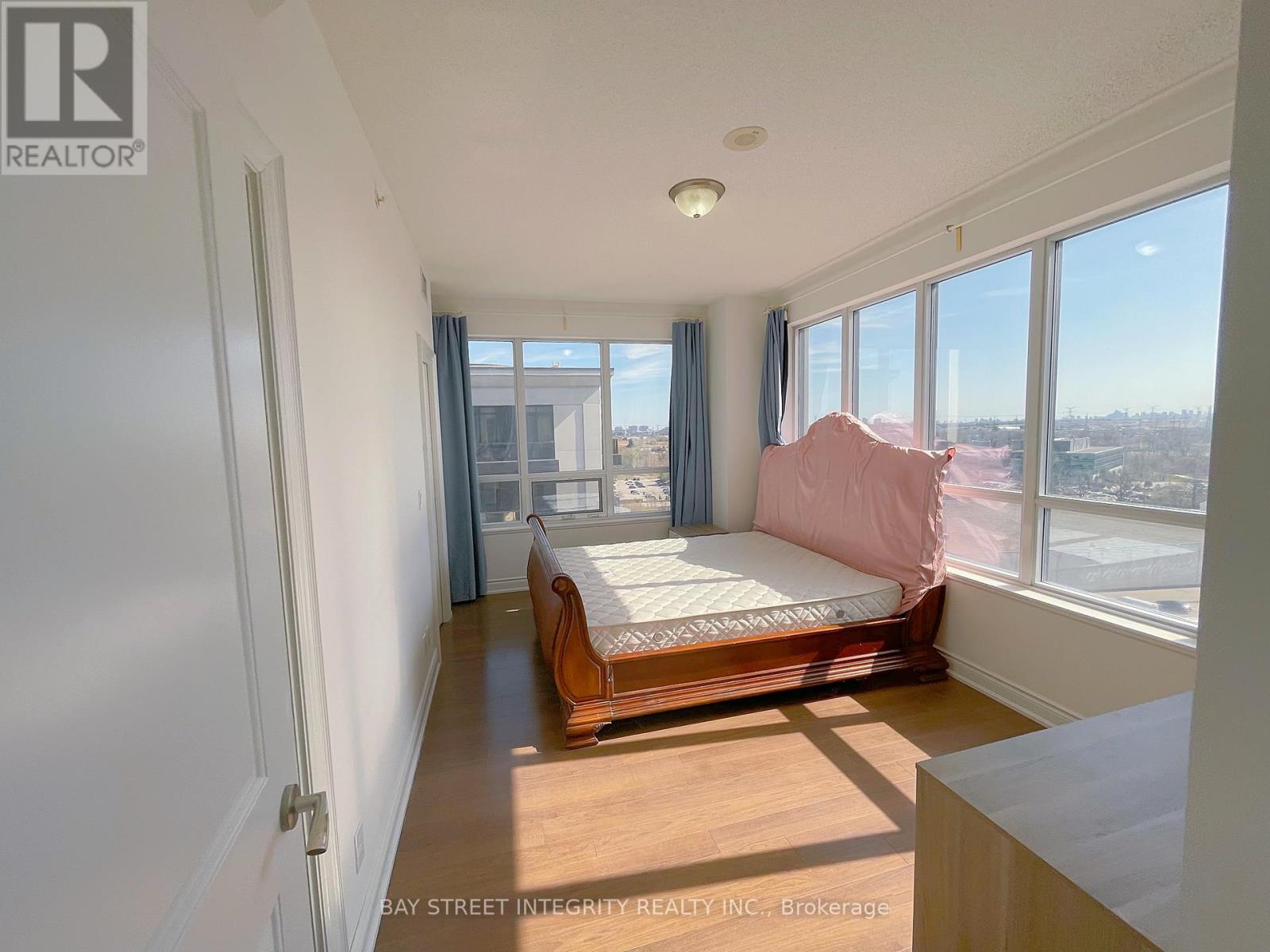 A bedroom with a bed, wooden floor, and a window overlooking a cityscape.
