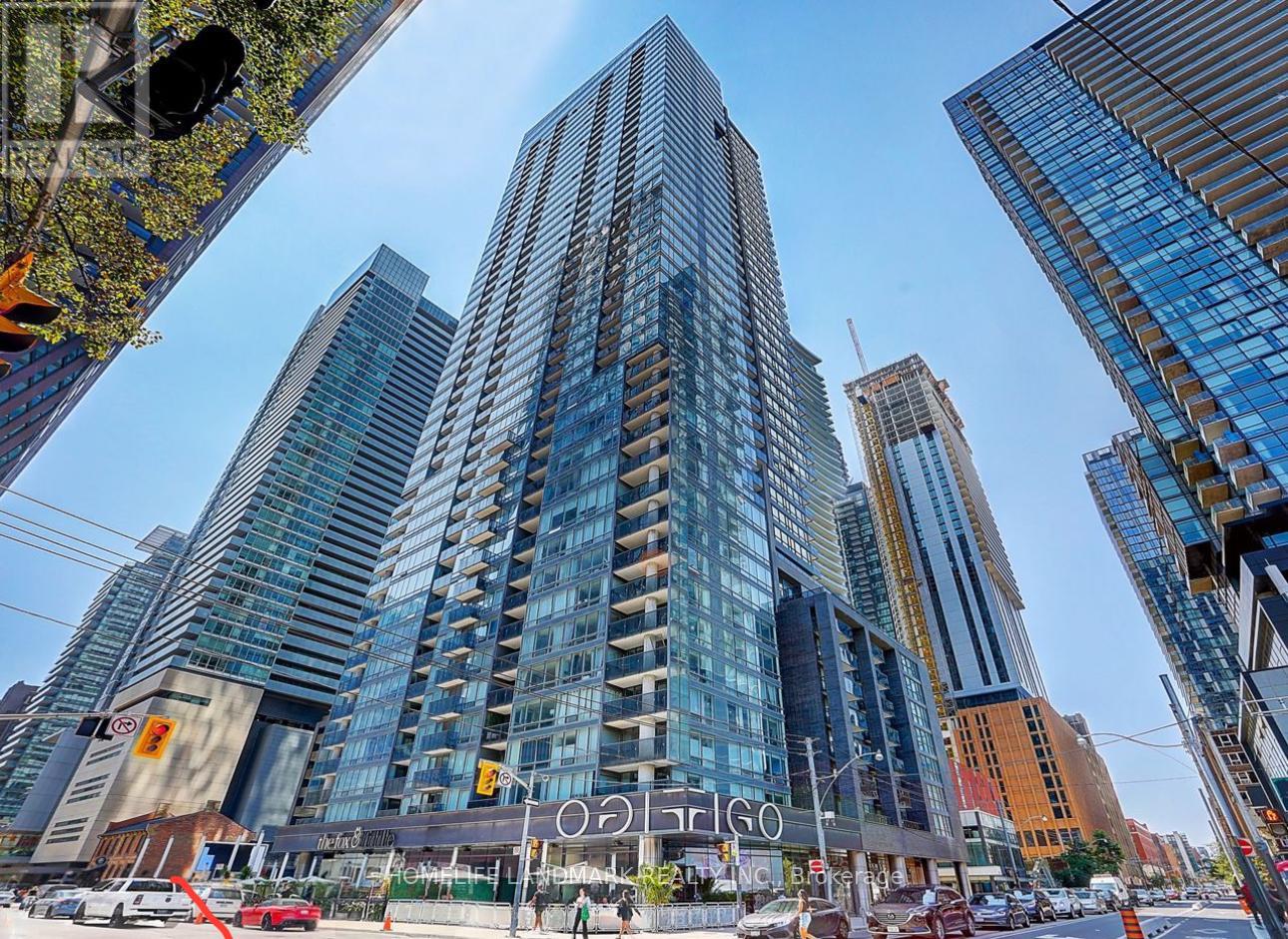 A tall building with a glass facade stands in the middle of a city street.