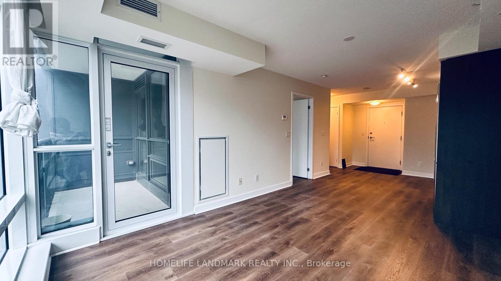 A spacious room with wooden floors and a glass door leading to a balcony.