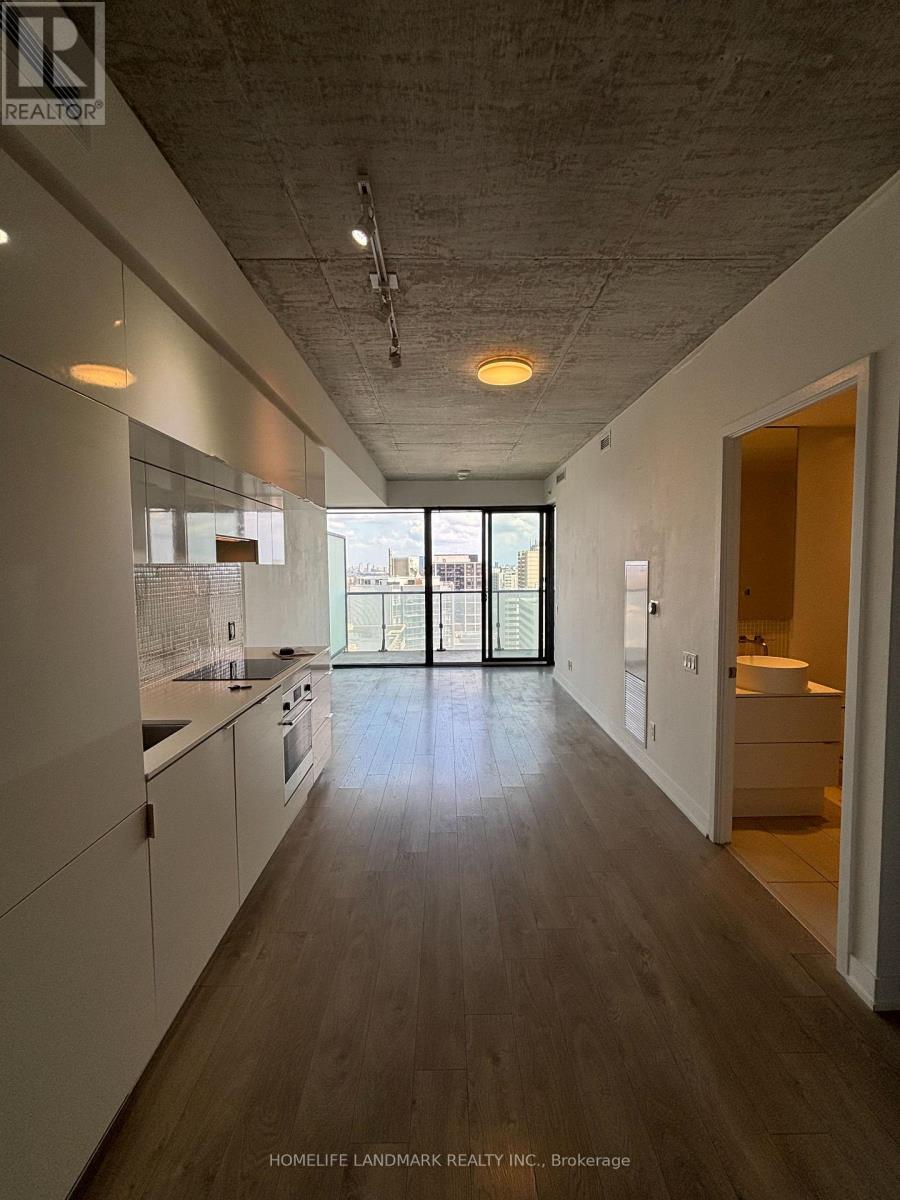 A long, narrow, white kitchen with wood floors and a view of the city outside the sliding glass doors.