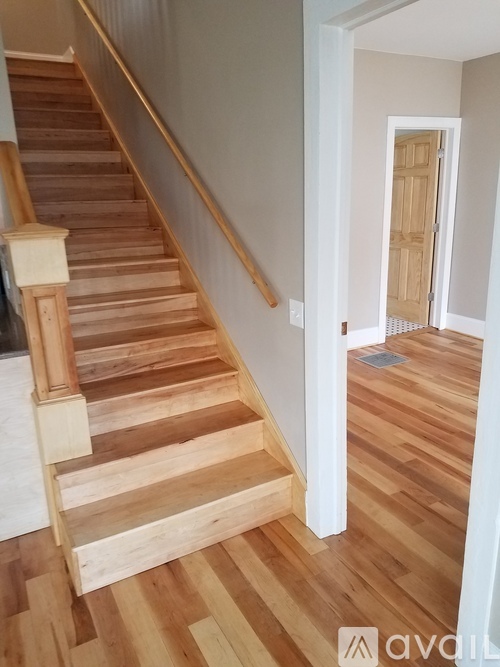 A wooden staircase with a white wall and a doorway.