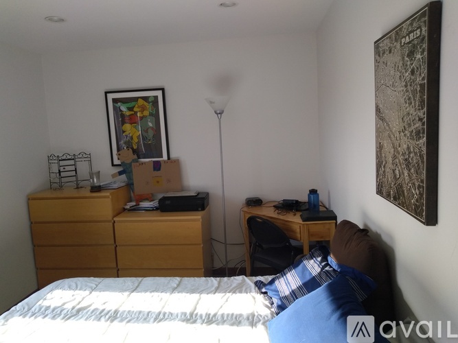A bedroom with a bed, desk, chair, and a painting on the wall.