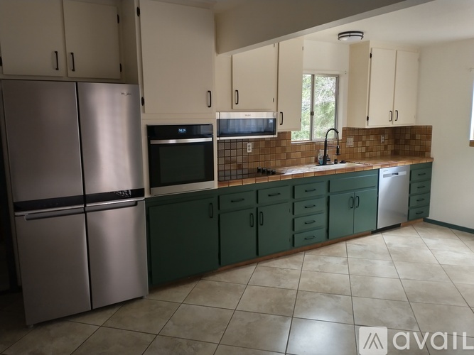A kitchen with a stainless steel refrigerator and green cabinets.