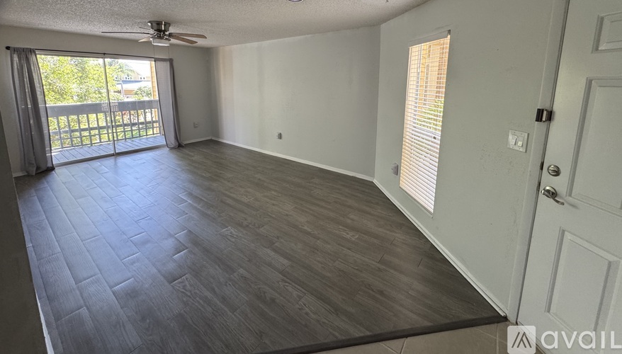 A spacious room with wooden flooring and a sliding glass door leading to a balcony.