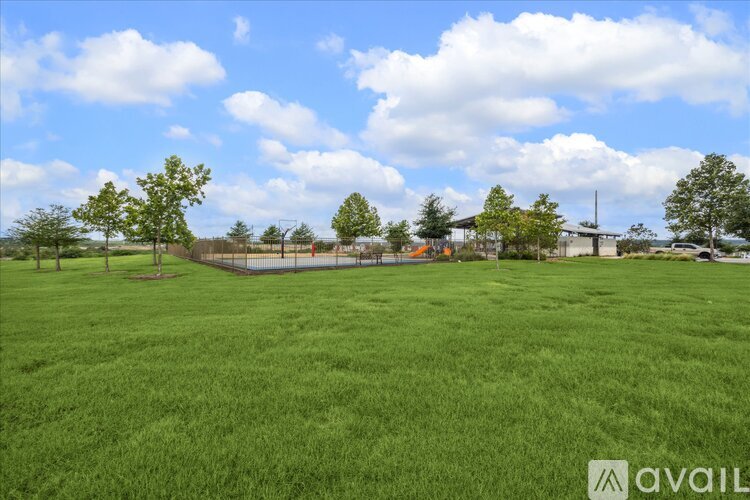A grassy field with trees and a building in the distance.
