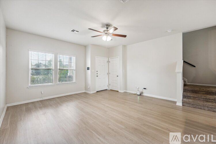 A spacious room with a ceiling fan and light, hardwood flooring, and a door leading to another room.