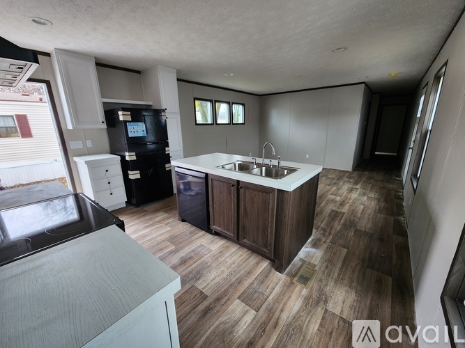 A kitchen with a black refrigerator, a sink, and wooden flooring.
