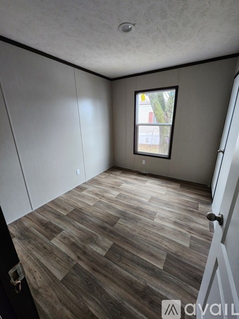 A room with wooden flooring and a window showing a tree and a building outside.