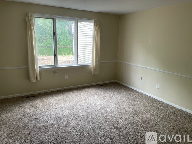 A room with a carpeted floor and a window with white curtains.
