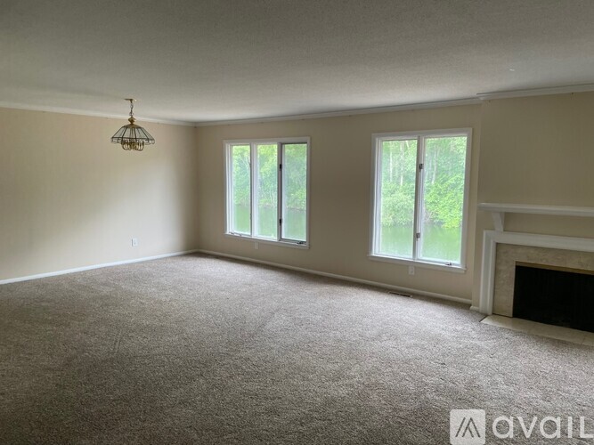 A room with a carpeted floor, a fireplace, and two windows.
