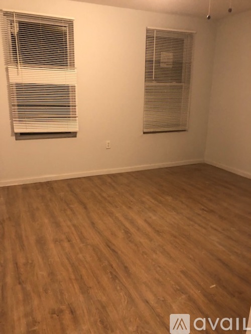 A room with wooden flooring and two windows with blinds.