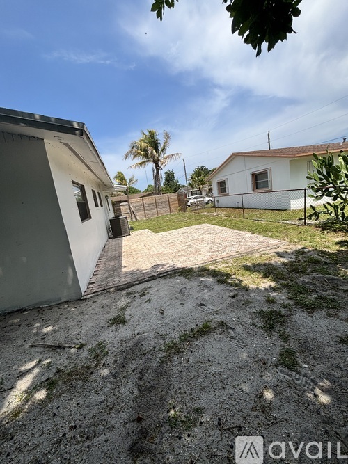 A house with a white fence and a grey building with a brown roof.
