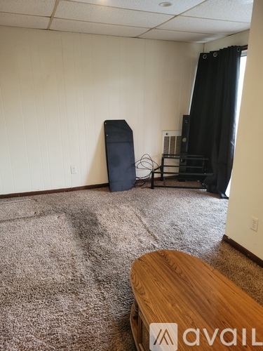 A room with a carpet, a wooden table, and a TV.