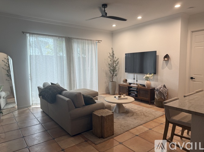 A living room with a grey couch, a white coffee table, and a flat screen TV mounted on the wall.