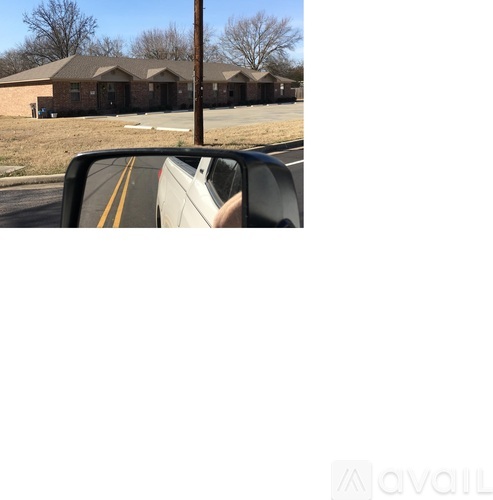 A car's side mirror is reflecting a building with a brown roof.
