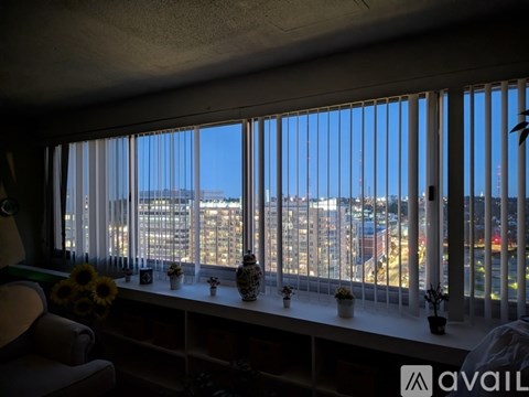 A room with a view of the city through a window with blinds.