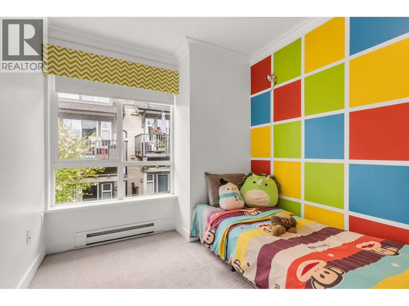 A bedroom with a colorful wall and a window overlooking a balcony.