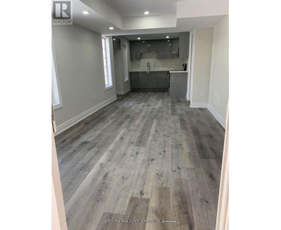 A spacious room with wooden flooring and a kitchen area in the background.