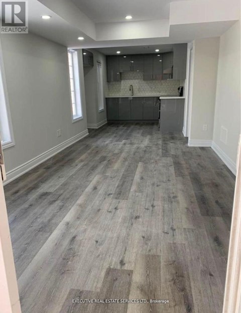 A spacious room with wooden flooring and a kitchen area in the background.