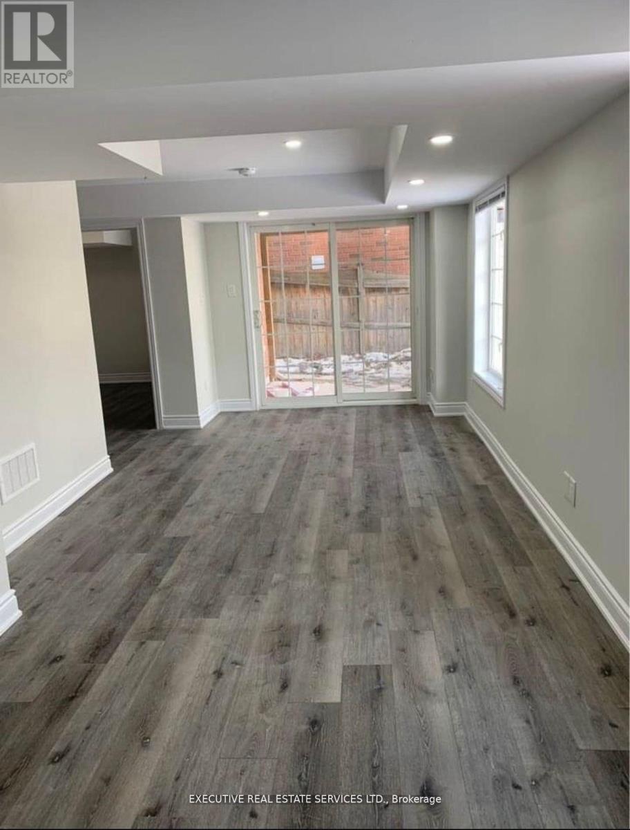 A room with wooden flooring and a window overlooking a fence.
