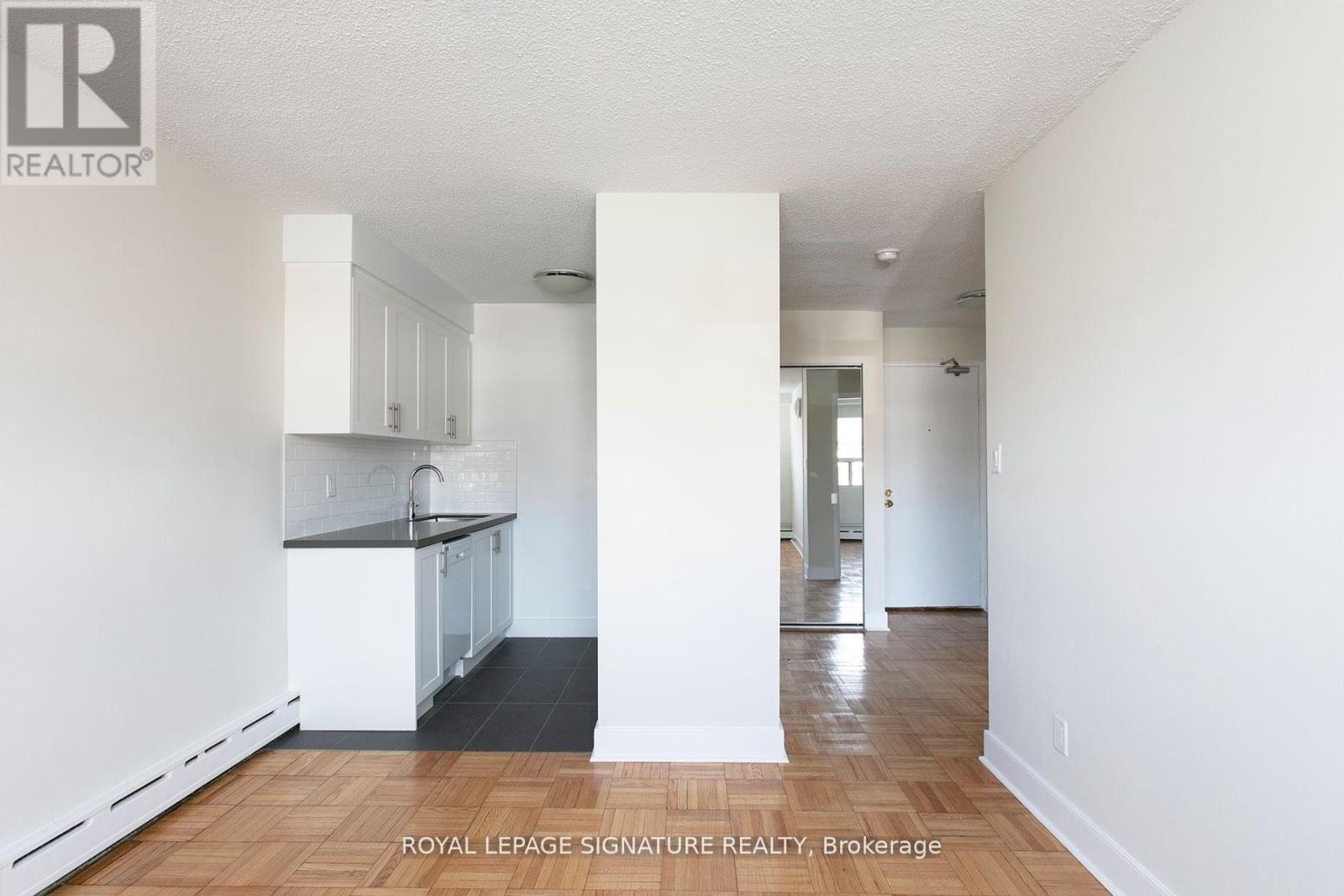A white interior of a room with a kitchen area and a hallway.