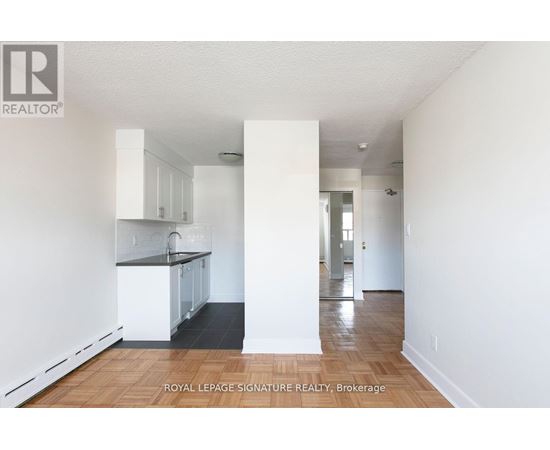 A white interior of a room with a kitchen area and a hallway.