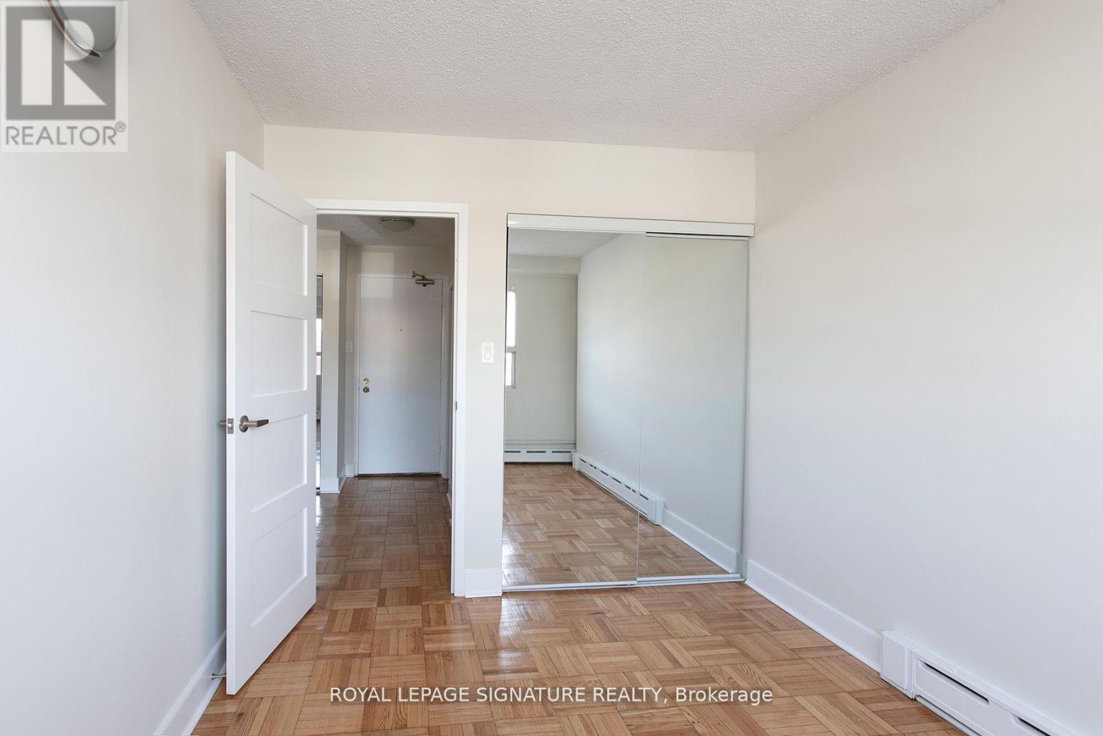 A white hallway with a door on the left and a mirror on the right.