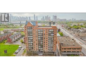 A tall brick building with a green roof is in the foreground with a city skyline in the background.
