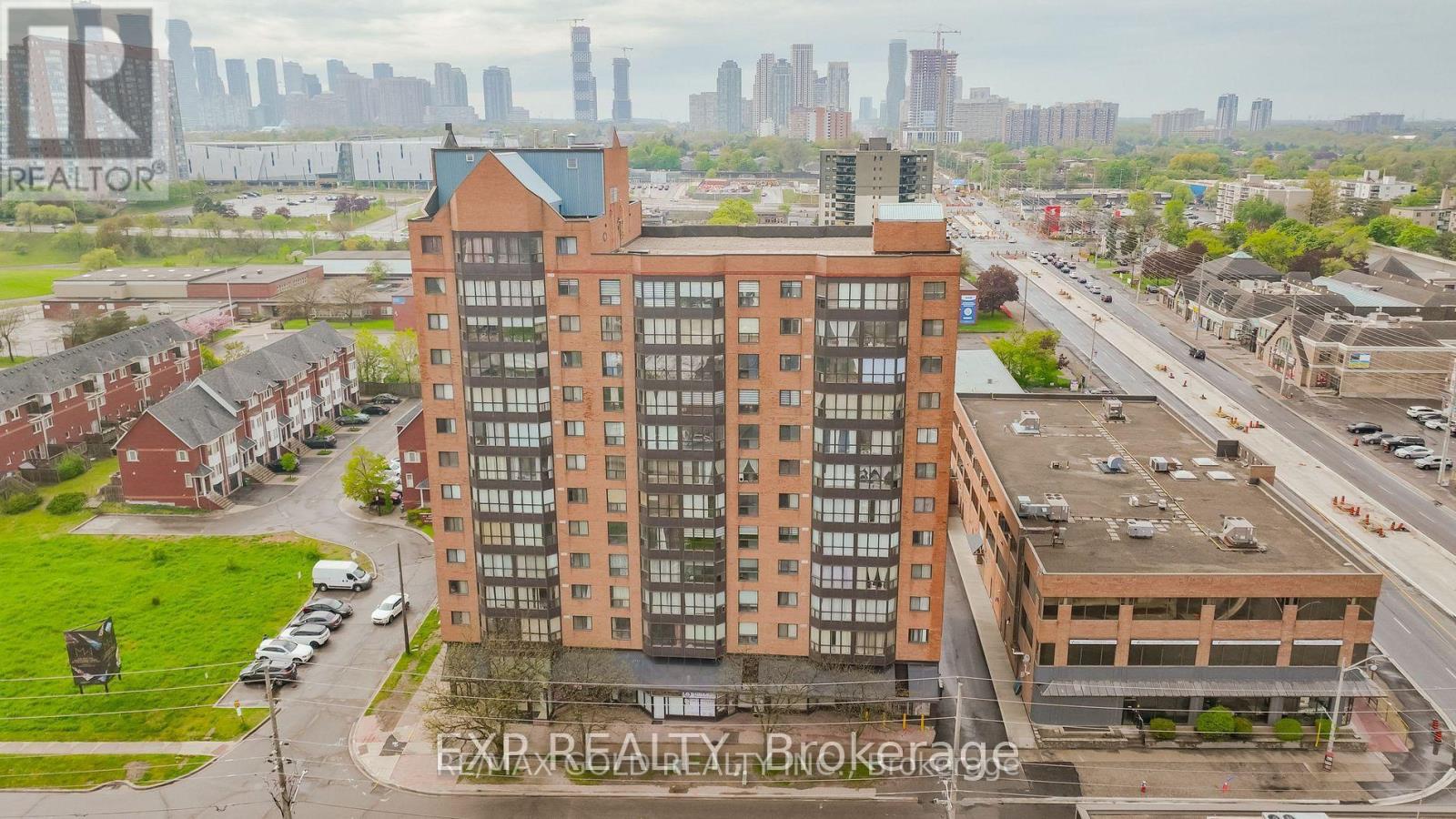 A large brick building with many windows is in the foreground of a city street.