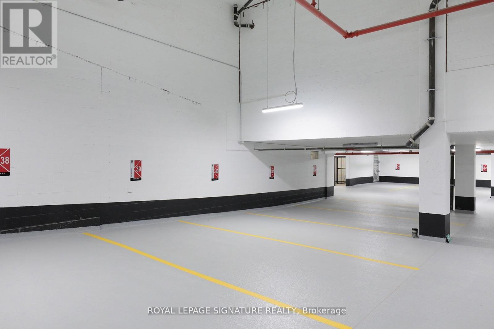 A spacious garage with yellow lines on the floor and red pipes on the ceiling.