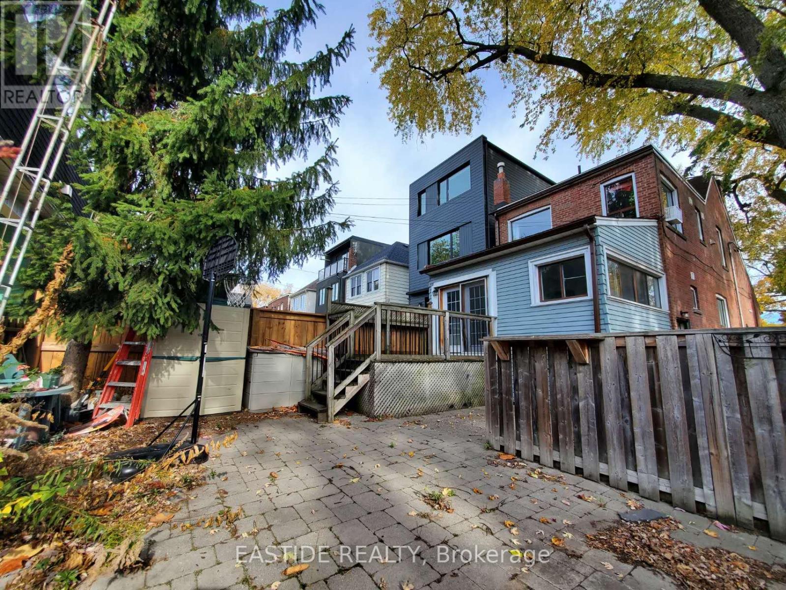 A tree-lined street with a wooden fence and a house with a grey roof.