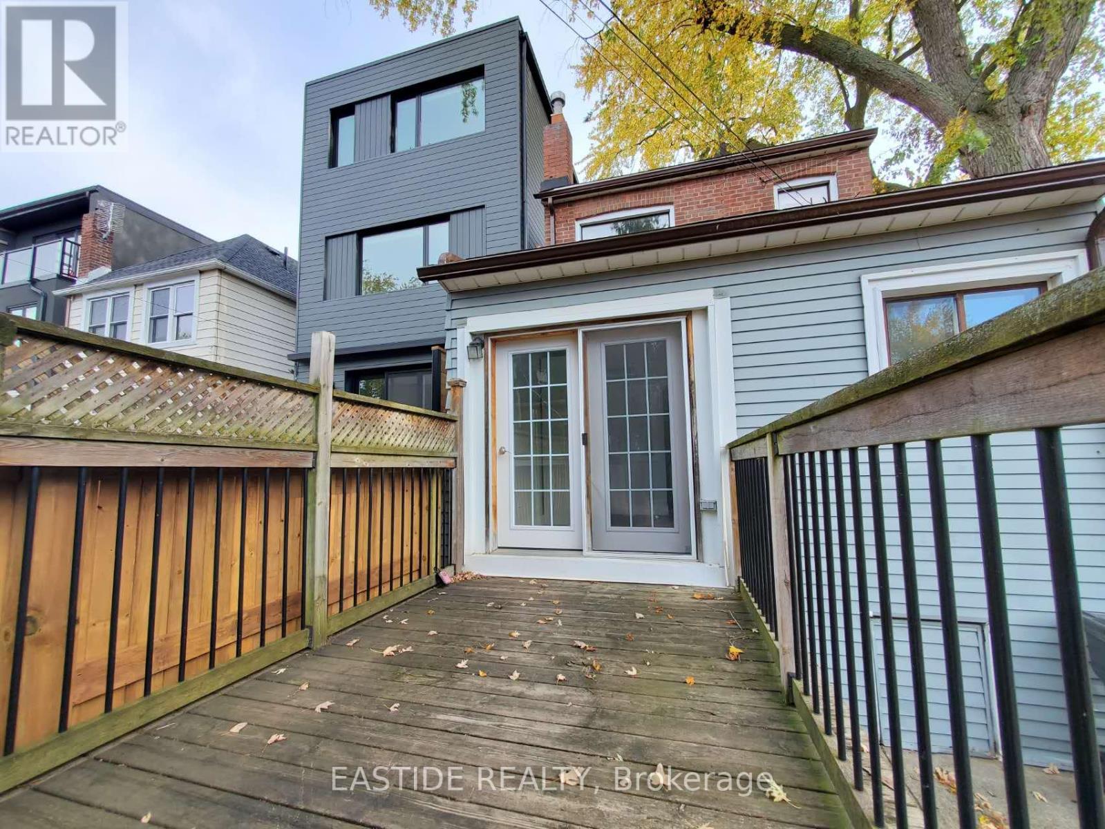 A wooden deck leads to a grey house with a glass door.