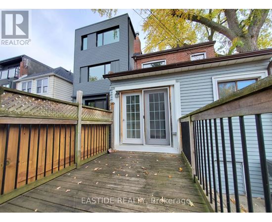 A wooden deck leads to a grey house with a glass door.