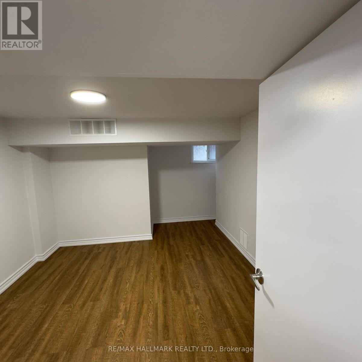 A room with wooden flooring and white walls, with a door on the right side.