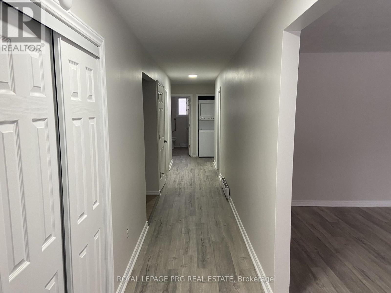 A long hallway with white doors on the left and wood flooring.