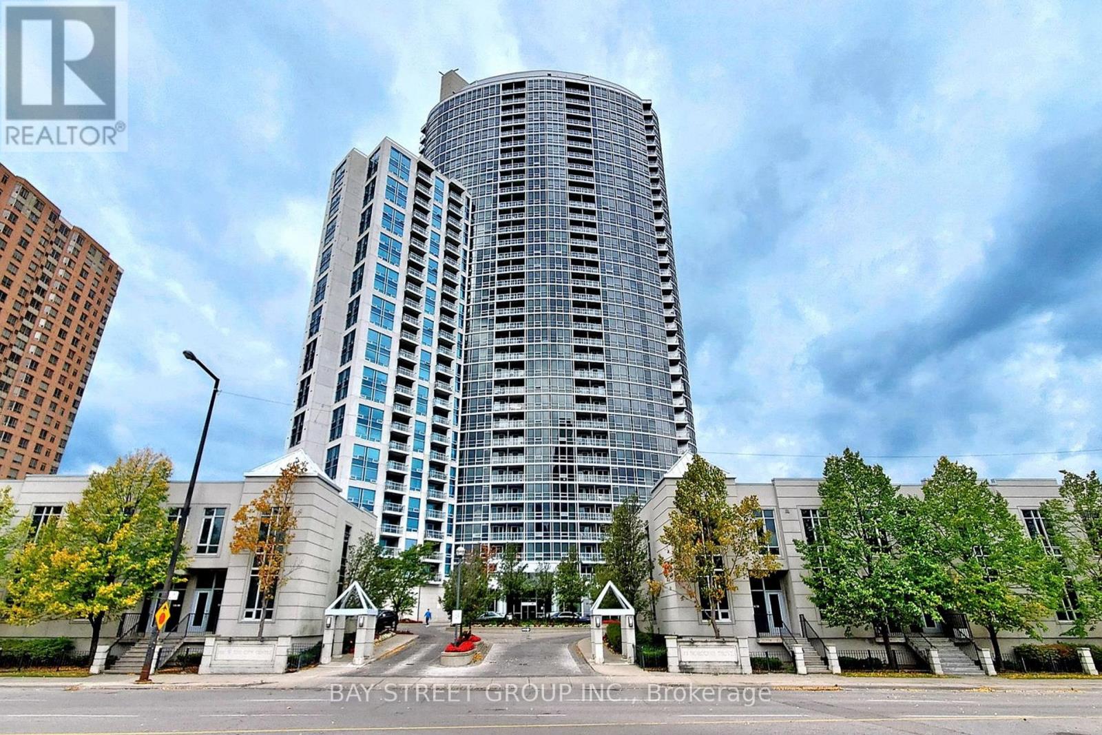A tall building with a glass facade stands in front of a row of trees.