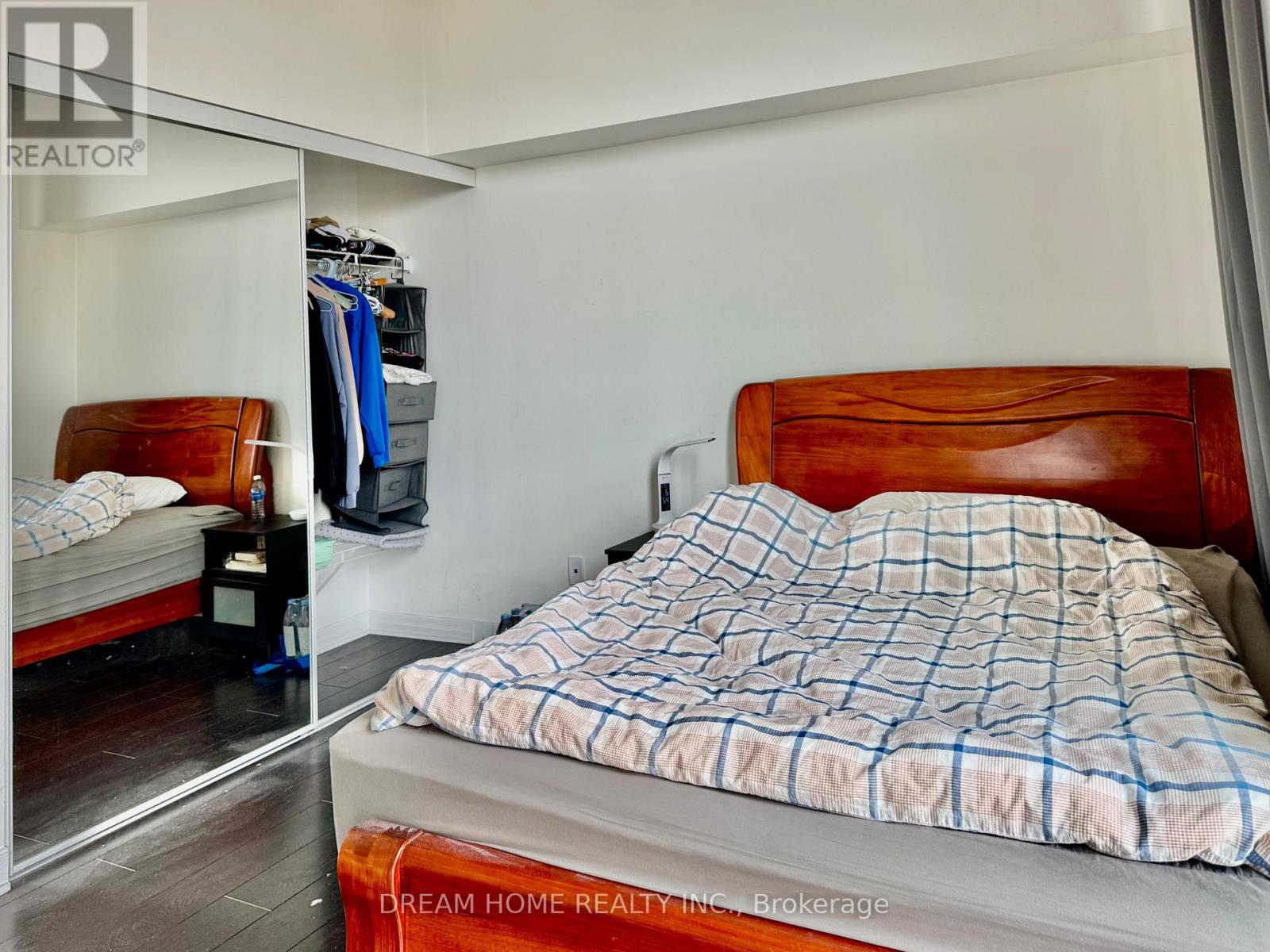 A bedroom with a bed, a nightstand, and a closet with clothes hanging.