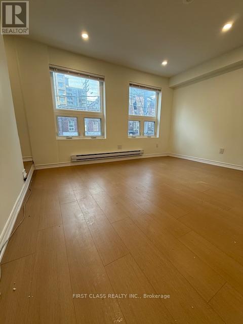 A room with wooden flooring and two windows.