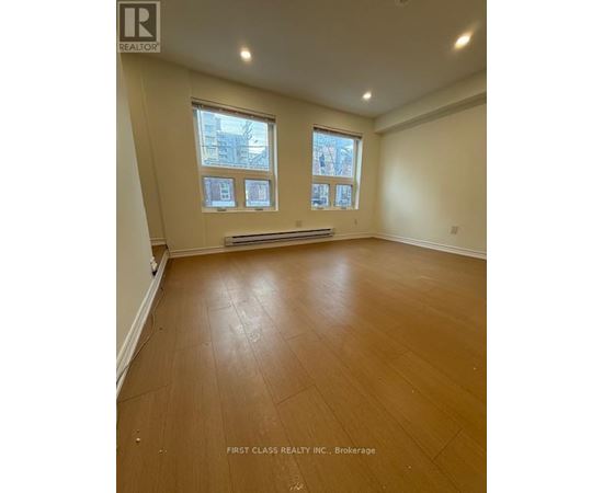 A room with wooden flooring and two windows.