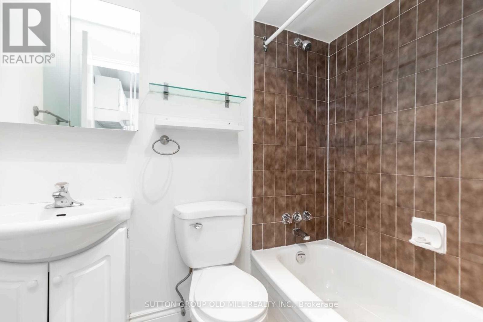 A white toilet sits in a bathroom with brown tiles.