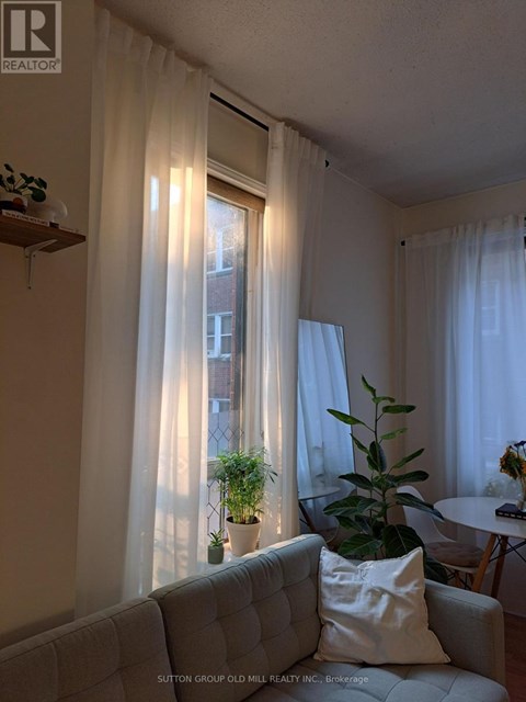 A living room with a grey couch and a window with white curtains.