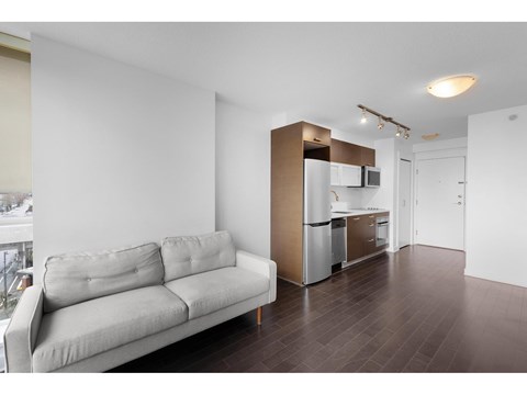 A modern living room with a grey couch and a kitchen area in the background.