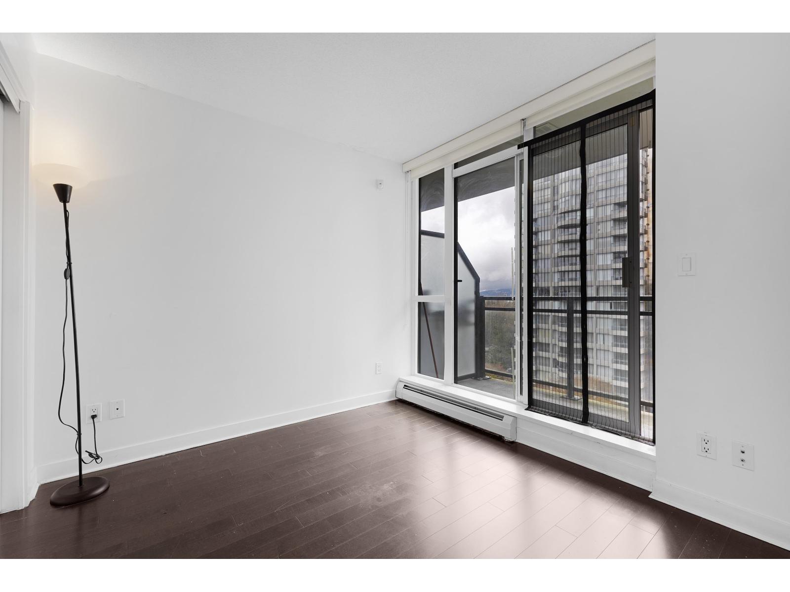 A room with a floor lamp and a window with a view of a building outside.