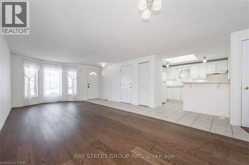 A spacious room with wooden flooring and white walls, with a dining area visible in the background.