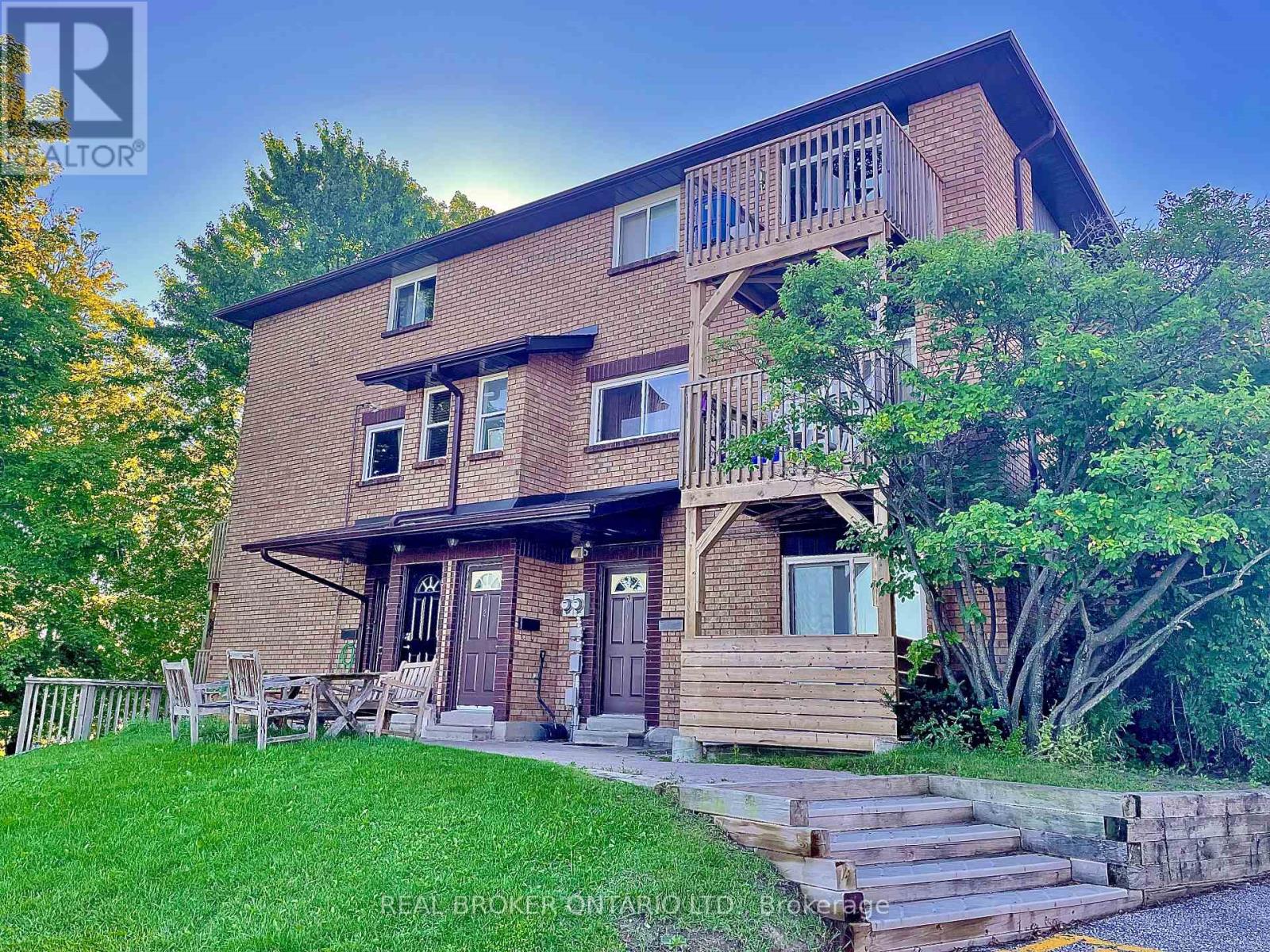 A house with a balcony and a deck is surrounded by greenery.