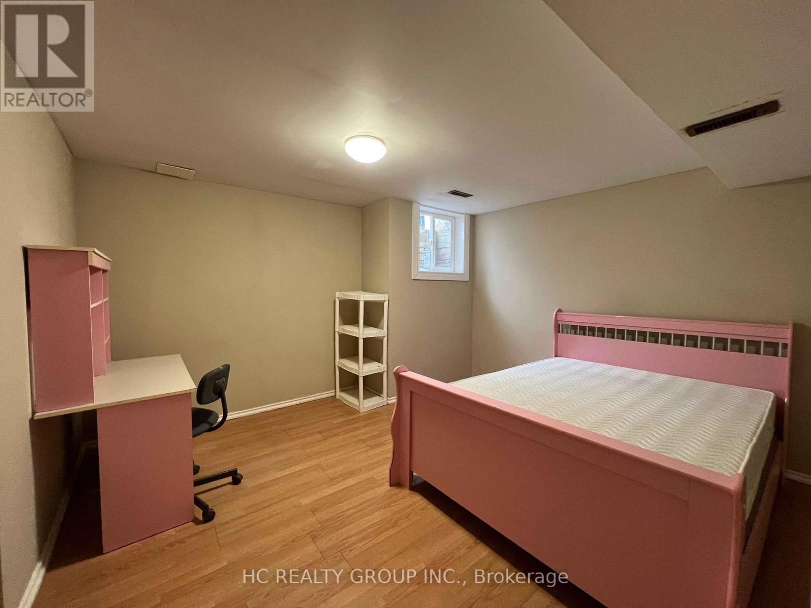 A bedroom with a pink bed and a desk with a chair.