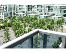 A balcony overlooks a courtyard with trees and a building in the background.