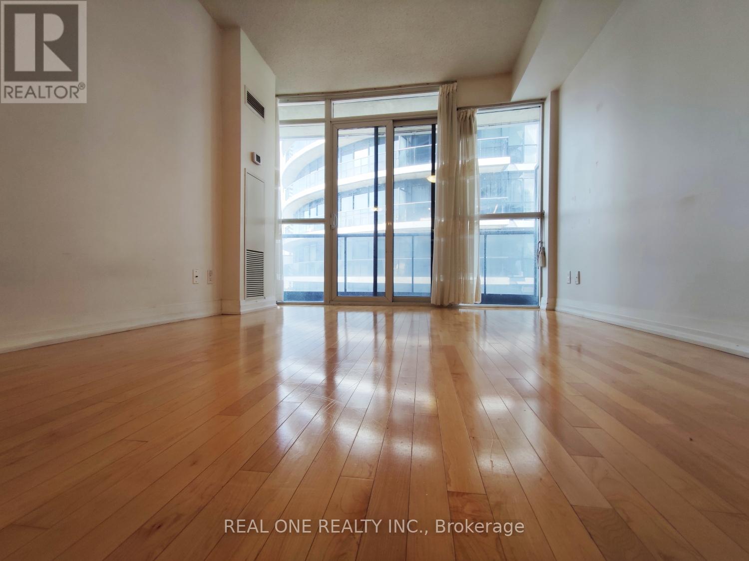 A room with wooden floors and a large window with a view of a building outside.