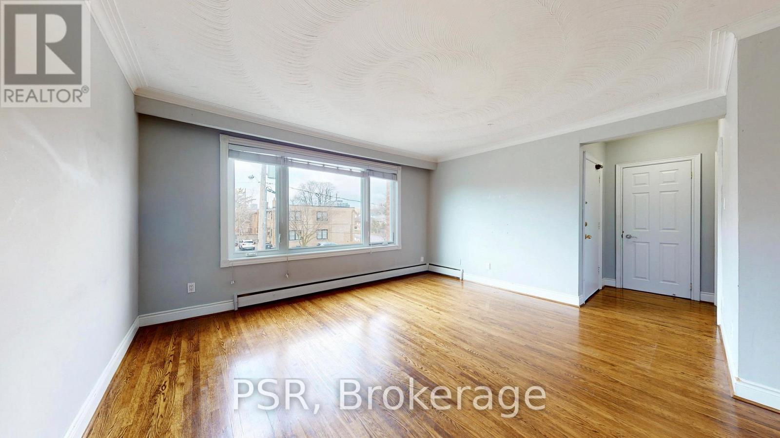 A room with wooden floors and a large window with a view of buildings outside.